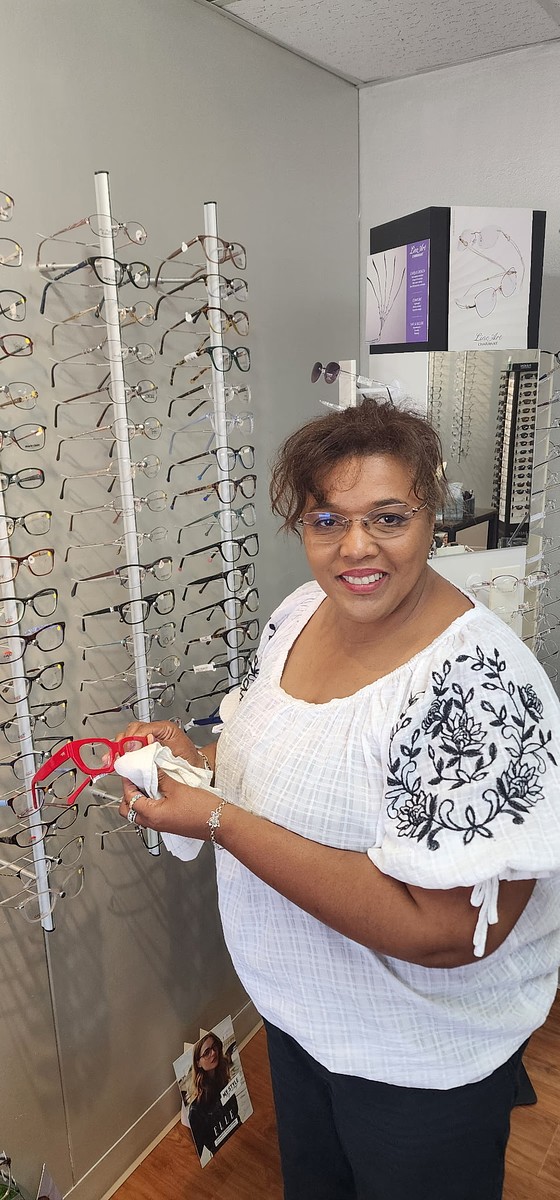 Andrea Baker cleaning a pair of red eyeglass frames in front of the frame wall at her Burnet, TX optical shop